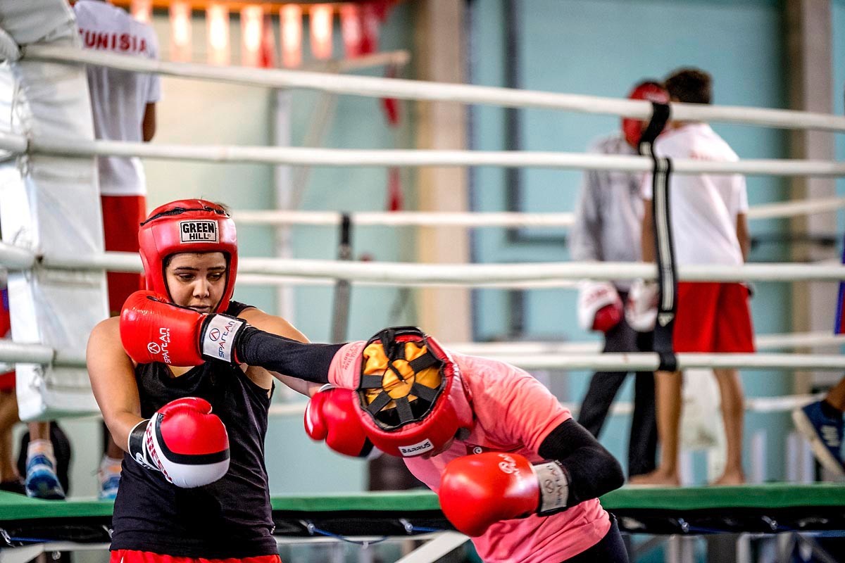Direct au visage lors d'un assaut sur le ring, la salle en activité derrière.