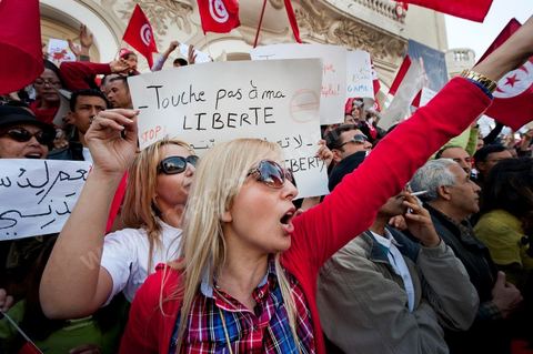 March 20, 2012: Nearly 6,000 Tunisians gathered Tuesday on Bourguiba Avenue in Tunis to celebrate Independence Day and “defend democracy” against “reactionary” forces, amid tensions fueled by the debate over identity and the role of religion.Tunisian flags were everywhere, horns blared, and the national anthem rang out: the demonstrators, who had come in response to calls on social media and from civic movements, chanted, “The people want a secular state!” “No to reactionary thinking, no to the caliphate,” or “We will not let obscurantist forces steal our revolution.”
The slogans of the revolution—“work, freedom, dignity”—were also chanted in unison. “In the name of the worker and the farmer, we continue to fight,” proclaimed one banner, while another demanded “jobs, or the government’s resignation.”  The 56th anniversary of independence—achieved on March 20, 1956, after 75 years of French protectorate rule—is taking place against a delicate backdrop, marked by growing tensions between the “Islamist” camp—which won the elections—and the “modernist” camp. The debate, exacerbated by incidents linked to Salafist radicals, centers on the question of Tunisian identity and the role religion should play in the country’s future constitution.