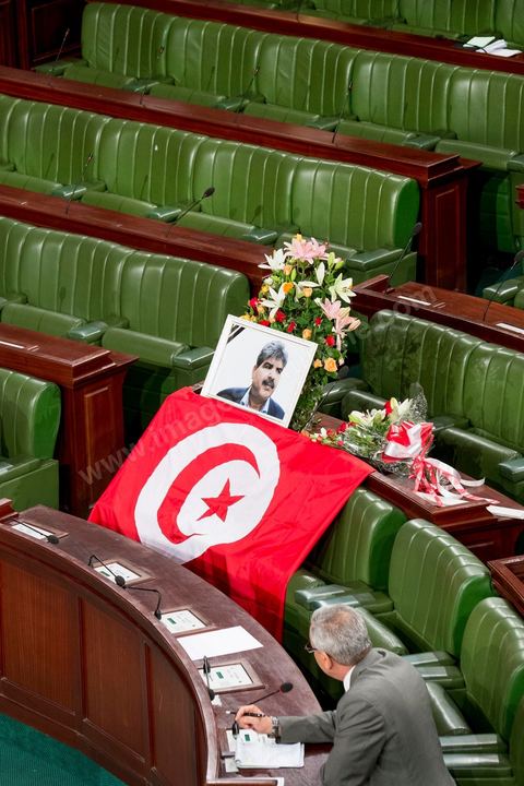 06 août 2013 : en place du siège du député assassiné  Mohamed Brahmi, des gerbes, son portrait et un drapeau national à la première séance de l'Assemblée depuis l'assassinat du député Mohamed Brahmi. La séance plénière débute par un long hommage au martyr avec prières et discours en présence des députés, hormis les 57 en retrait, du Premier Ministre et des ministres de l'Intérieur et de la Défense qui par leurs discours exposeront la situation dans le pays.