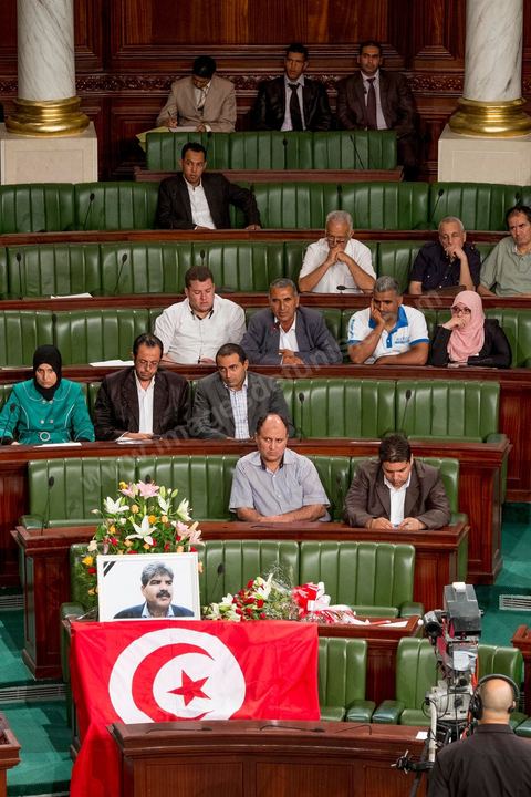 06 août 2013 : en place du siège du député assassiné  Mohamed Brahmi, des gerbes, son portrait et un drapeau national à la première séance de l'Assemblée depuis l'assassinat du député Mohamed Brahmi. La séance plénière débute par un long hommage au martyr avec prières et discours en présence des députés, hormis les 57 en retrait, du Premier Ministre et des ministres de l'Intérieur et de la Défense qui par leurs discours exposeront la situation dans le pays.