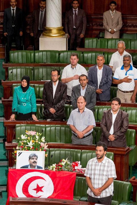 06 août 2013 : en place du siège du député assassiné  Mohamed Brahmi, des gerbes, son portrait et un drapeau national à la première séance de l'Assemblée depuis l'assassinat du député Mohamed Brahmi. La séance plénière débute par un long hommage au martyr avec prières et discours en présence des députés, hormis les 57 en retrait, du Premier Ministre et des ministres de l'Intérieur et de la Défense qui par leurs discours exposeront la situation dans le pays.