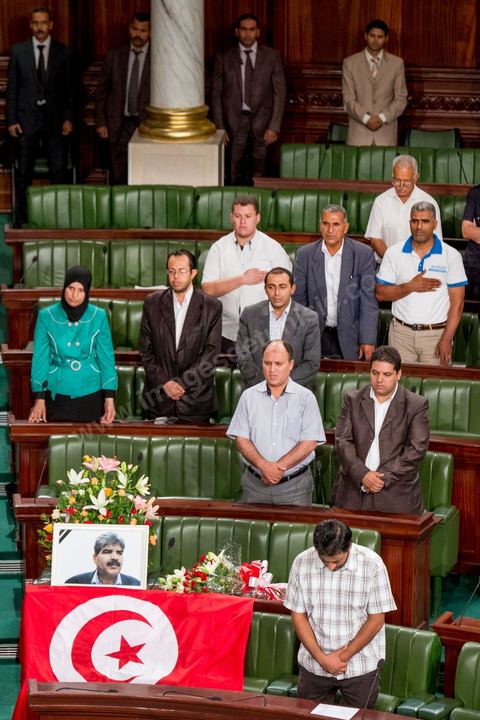 06 août 2013 : en place du siège du député assassiné  Mohamed Brahmi, des gerbes, son portrait et un drapeau national à la première séance de l'Assemblée depuis l'assassinat du député Mohamed Brahmi. La séance plénière débute par un long hommage au martyr avec prières et discours en présence des députés, hormis les 57 en retrait, du Premier Ministre et des ministres de l'Intérieur et de la Défense qui par leurs discours exposeront la situation dans le pays.