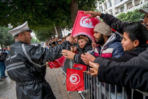 14 janvier 2014 : Un policier distribue des drapeau tunisien aux passants sur l'avenue Habib Bourguiba à Tunis quelques milliers de tunisiens sont venus se rassembler pour commémorer le troisième anniversaire du départ de l'ancien Président Ben Ali, aboutissement des mouvements de révoltes en région démarrés le 17 décmbre 2010. Tous les genres politiques se croisent et se chamaillent l'avenue, d'un côté les islamistes avec Ennahdha, les ligues et même un nouveau mouvement islamiste anachiste, de l'autre la gauche et l'opposition commémorant à la fois le départ des anciens et la mémoire des martyrs de la révolution et des martyrs politiques. 