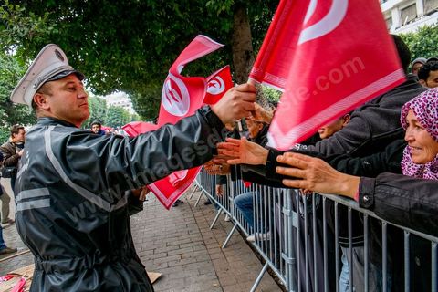 14 janvier 2014 : Un policier distribue des drapeau tunisien aux passants sur l'avenue Habib Bourguiba à Tunis quelques milliers de tunisiens sont venus se rassembler pour commémorer le troisième anniversaire du départ de l'ancien Président Ben Ali, aboutissement des mouvements de révoltes en région démarrés le 17 décmbre 2010. Tous les genres politiques se croisent et se chamaillent l'avenue, d'un côté les islamistes avec Ennahdha, les ligues et même un nouveau mouvement islamiste anachiste, de l'autre la gauche et l'opposition commémorant à la fois le départ des anciens et la mémoire des martyrs de la révolution et des martyrs politiques. 