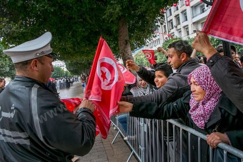 14 janvier 2014 : Un policier distribue des drapeau tunisien aux passants sur l'avenue Habib Bourguiba à Tunis quelques milliers de tunisiens sont venus se rassembler pour commémorer le troisième anniversaire du départ de l'ancien Président Ben Ali, aboutissement des mouvements de révoltes en région démarrés le 17 décmbre 2010. Tous les genres politiques se croisent et se chamaillent l'avenue, d'un côté les islamistes avec Ennahdha, les ligues et même un nouveau mouvement islamiste anachiste, de l'autre la gauche et l'opposition commémorant à la fois le départ des anciens et la mémoire des martyrs de la révolution et des martyrs politiques. 