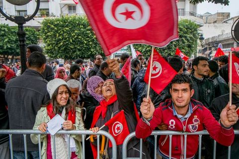 14 janvier 2014 : Un policier distribue des drapeau tunisien aux passants sur l'avenue Habib Bourguiba à Tunis quelques milliers de tunisiens sont venus se rassembler pour commémorer le troisième anniversaire du départ de l'ancien Président Ben Ali, aboutissement des mouvements de révoltes en région démarrés le 17 décmbre 2010. Tous les genres politiques se croisent et se chamaillent l'avenue, d'un côté les islamistes avec Ennahdha, les ligues et même un nouveau mouvement islamiste anachiste, de l'autre la gauche et l'opposition commémorant à la fois le départ des anciens et la mémoire des martyrs de la révolution et des martyrs politiques. 