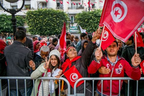 14 janvier 2014 : Un policier distribue des drapeau tunisien aux passants sur l'avenue Habib Bourguiba à Tunis quelques milliers de tunisiens sont venus se rassembler pour commémorer le troisième anniversaire du départ de l'ancien Président Ben Ali, aboutissement des mouvements de révoltes en région démarrés le 17 décmbre 2010. Tous les genres politiques se croisent et se chamaillent l'avenue, d'un côté les islamistes avec Ennahdha, les ligues et même un nouveau mouvement islamiste anachiste, de l'autre la gauche et l'opposition commémorant à la fois le départ des anciens et la mémoire des martyrs de la révolution et des martyrs politiques. 