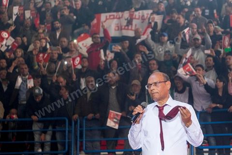 14 décembre 2014 : Au milieu de son speech, deux jeunes femmes sont arrivées sur le podium en ramenant un cadeau au candidat au second tour de l’élection présidentielle une cravate rouge ! Connu pour avoir toujours refusé de porter de cravate, afin de ne pas rompre son élan populiste, Moncef Marzouki a accepté le cadeau des deux jeunes filles et l’a même porté sur le champ. Grand meeting de Moncef Marzouki qui fait salle comble à la coupole de Tunis à une semaine du 2d tour des élections présidentielles. Moncef Marzouki, a appelé ses partisans, « à ne pas tomber dans le piège des insultes et à ne pas dire du mal de son rival Béji Caid Essebsi », tout en affirmant «nous avons le droit de juger cet homme pour son passé et pour son rôle destructeur au cours de la phase transitoire…, mais notre combat est celui des valeurs et l’éthique».Le président sortant et candidat au second tour de la présidentielle a tenu dimanche un meeting au palais des sports d’El Menzah. Ses partisans venus des différentes régions du pays ont scandé des slogans hostiles à son rival Béji Caid Essebsi et à son parti Nidaa Tounes.