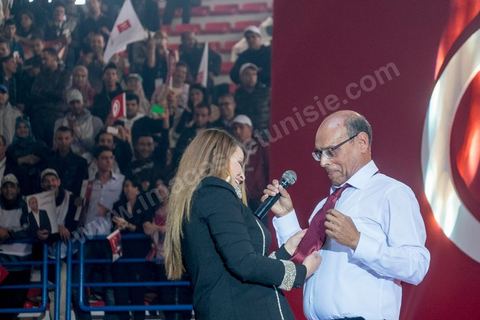 14 décembre 2014 : Au milieu de son speech, deux jeunes femmes sont arrivées sur le podium en ramenant un cadeau au candidat au second tour de l’élection présidentielle une cravate rouge ! Connu pour avoir toujours refusé de porter de cravate, afin de ne pas rompre son élan populiste, Moncef Marzouki a accepté le cadeau des deux jeunes filles et l’a même porté sur le champ. Grand meeting de Moncef Marzouki qui fait salle comble à la coupole de Tunis à une semaine du 2d tour des élections présidentielles. Moncef Marzouki, a appelé ses partisans, « à ne pas tomber dans le piège des insultes et à ne pas dire du mal de son rival Béji Caid Essebsi », tout en affirmant «nous avons le droit de juger cet homme pour son passé et pour son rôle destructeur au cours de la phase transitoire…, mais notre combat est celui des valeurs et l’éthique».Le président sortant et candidat au second tour de la présidentielle a tenu dimanche un meeting au palais des sports d’El Menzah. Ses partisans venus des différentes régions du pays ont scandé des slogans hostiles à son rival Béji Caid Essebsi et à son parti Nidaa Tounes.