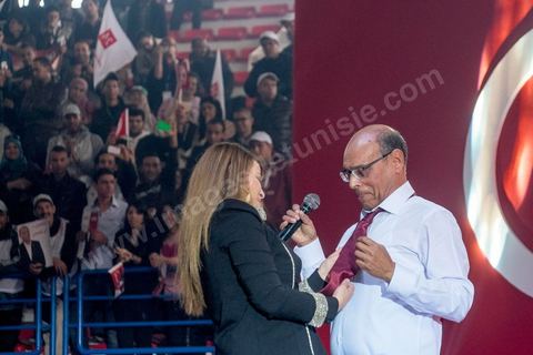 14 décembre 2014 : Au milieu de son speech, deux jeunes femmes sont arrivées sur le podium en ramenant un cadeau au candidat au second tour de l’élection présidentielle une cravate rouge ! Connu pour avoir toujours refusé de porter de cravate, afin de ne pas rompre son élan populiste, Moncef Marzouki a accepté le cadeau des deux jeunes filles et l’a même porté sur le champ. Grand meeting de Moncef Marzouki qui fait salle comble à la coupole de Tunis à une semaine du 2d tour des élections présidentielles. Moncef Marzouki, a appelé ses partisans, « à ne pas tomber dans le piège des insultes et à ne pas dire du mal de son rival Béji Caid Essebsi », tout en affirmant «nous avons le droit de juger cet homme pour son passé et pour son rôle destructeur au cours de la phase transitoire…, mais notre combat est celui des valeurs et l’éthique».Le président sortant et candidat au second tour de la présidentielle a tenu dimanche un meeting au palais des sports d’El Menzah. Ses partisans venus des différentes régions du pays ont scandé des slogans hostiles à son rival Béji Caid Essebsi et à son parti Nidaa Tounes.