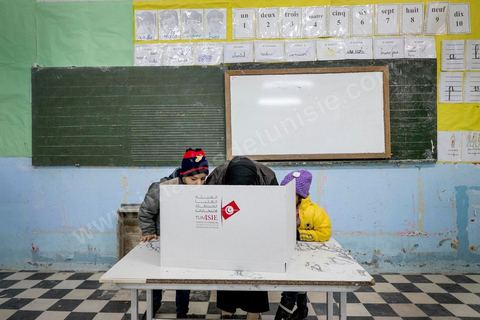 21 décembre 2014 : Accompagnée de ses enfants, une habitante accomplit son devoir civique. jour de vote pour le second tour des élections présidentielles opposant Beji Caid Essebsi, favori,  au président sortant Moncef Marzouki.