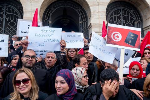 6 décémbre 2016 : Plus de 2.000 avocats ont manifesté mardi à Tunis contre les nouvelles dispositions fiscales qui leur ont été imposées dans le projet de budget 2017, actuellement examiné par le Parlement."Avec notre âme, avec notre sang nous défendrons le métier d'avocat", ont crié les manifestants en robe noire devant le siège du gouvernement à la Kasbah, dans le centre de Tunis, après une marche de quelques centaines de mètres."Les avocats sont en colère!", "Nous n'allons pas financer votre corruption", pouvait-on lire sur des pancartes brandies par les protestataires, dont beaucoup jugent les nouvelles mesures "injustes" et "inapplicables".En cause, des taxes imposées pour chaque dossier traité, pouvant être déduites de l'impôt sur le revenu et prévues dans le projet de loi de finances 2017.Ce mouvement ne fait toutefois pas l'unanimité, et sur les réseaux sociaux comme dans certains médias, les protestations des avocats ont été considérées comme une volonté de bénéficier d'un traitement spécial. Selon le webzine Inkyfada, qui a analysé des données officielles, 60% des avocats enregistrés n'ont pas déclaré d'impôts en 2015, et "les avocats en règle paient en moyenne 228 dinars (92 euros) d'impôt sur le revenu par mois".