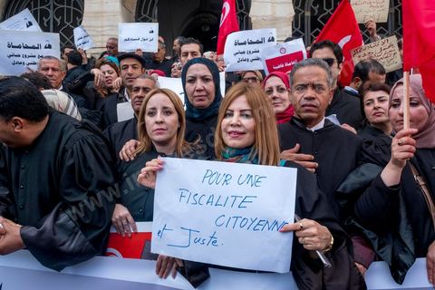 6 décémbre 2016 : Plus de 2.000 avocats ont manifesté mardi à Tunis contre les nouvelles dispositions fiscales qui leur ont été imposées dans le projet de budget 2017, actuellement examiné par le Parlement."Avec notre âme, avec notre sang nous défendrons le métier d'avocat", ont crié les manifestants en robe noire devant le siège du gouvernement à la Kasbah, dans le centre de Tunis, après une marche de quelques centaines de mètres."Les avocats sont en colère!", "Nous n'allons pas financer votre corruption", pouvait-on lire sur des pancartes brandies par les protestataires, dont beaucoup jugent les nouvelles mesures "injustes" et "inapplicables".En cause, des taxes imposées pour chaque dossier traité, pouvant être déduites de l'impôt sur le revenu et prévues dans le projet de loi de finances 2017.Ce mouvement ne fait toutefois pas l'unanimité, et sur les réseaux sociaux comme dans certains médias, les protestations des avocats ont été considérées comme une volonté de bénéficier d'un traitement spécial. Selon le webzine Inkyfada, qui a analysé des données officielles, 60% des avocats enregistrés n'ont pas déclaré d'impôts en 2015, et "les avocats en règle paient en moyenne 228 dinars (92 euros) d'impôt sur le revenu par mois".