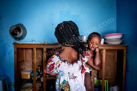 24 juin 2017 : Océane et son fils dans la cuisine. Chez Océane, migrante Ivoirienne à Tunis dans un quartier populaire. Elle vit dans une maison avec 2 chambres qu'elle partage avec son fils Eden et cinq autres ivoiriennes. Océane est arrivée en Tunisie en 2010 comme étudiante et est depuis 5 ans en situation irrégulière, ne lui permettant plus de travailler légalement. Il y a deux ans Eden est né, ce jeune garçon plein de joie est devenu sa raison de vivre, elle souhaite trouver un endroit pour vivre normalement et élever son fils. “J’estime que pour vivre bien Tunisie, il me faudrait entre 800 et 1000 dinars. Généralement, je suis plutôt à 350. Entre les couches et la nourriture, les dépenses sont rapides.” La jeune femme travaille de façon irrégulière : elle a quelques patrons qui l’appellent, selon leur besoin, pour faire le ménage chez eux. Une journée lui rapporte entre 25 et 30 dinars.  