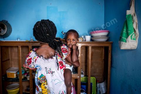 24 juin 2017 : Océane et son fils dans la cuisine. Chez Océane, migrante Ivoirienne à Tunis dans un quartier populaire. Elle vit dans une maison avec 2 chambres qu'elle partage avec son fils Eden et cinq autres ivoiriennes. Océane est arrivée en Tunisie en 2010 comme étudiante et est depuis 5 ans en situation irrégulière, ne lui permettant plus de travailler légalement. Il y a deux ans Eden est né, ce jeune garçon plein de joie est devenu sa raison de vivre, elle souhaite trouver un endroit pour vivre normalement et élever son fils. “J’estime que pour vivre bien Tunisie, il me faudrait entre 800 et 1000 dinars. Généralement, je suis plutôt à 350. Entre les couches et la nourriture, les dépenses sont rapides.” La jeune femme travaille de façon irrégulière : elle a quelques patrons qui l’appellent, selon leur besoin, pour faire le ménage chez eux. Une journée lui rapporte entre 25 et 30 dinars.  
