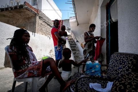 24 juin 2017 : Océane et son fils Eden dans la petite cour est le lieu de vie commune en cette péiode de grande chaleur. Chez Océane, migrante Ivoirienne à Tunis dans un quartier populaire. Elle vit dans une maison avec 2 chambres qu'elle partage avec son fils Eden et cinq autres ivoiriennes. Océane est arrivée en Tunisie en 2010 comme étudiante et est depuis 5 ans en situation irrégulière, ne lui permettant plus de travailler légalement. Il y a deux ans Eden est né, ce jeune garçon plein de joie est devenu sa raison de vivre, elle souhaite trouver un endroit pour vivre normalement et élever son fils. “J’estime que pour vivre bien Tunisie, il me faudrait entre 800 et 1000 dinars. Généralement, je suis plutôt à 350. Entre les couches et la nourriture, les dépenses sont rapides.” La jeune femme travaille de façon irrégulière : elle a quelques patrons qui l’appellent, selon leur besoin, pour faire le ménage chez eux. Une journée lui rapporte entre 25 et 30 dinars.  