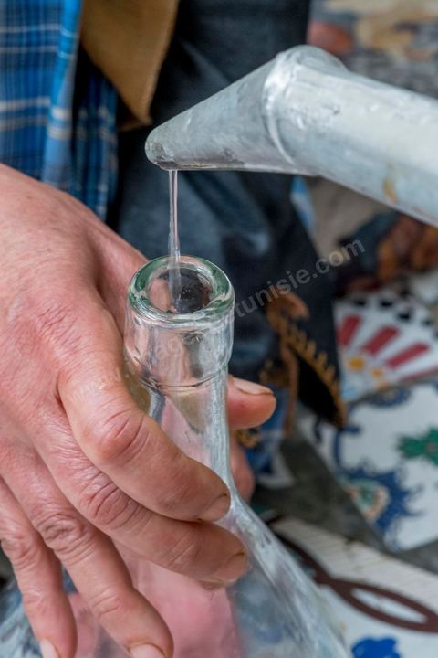 Distillation traditionnelle de fleurs de rose dans maison de la région de Nabeul au Cap Bon. L'eau et l'essence de rose proviennent de la distillation des fleurs de rose. La distillation est conduite très doucement sur le feu, l'hydrolat coule dans des Marie-Jeannes en verre. Le distillat coule légèrement tiède. 1 kg de pétale produit environ 1,5 litres d'eau de roses.