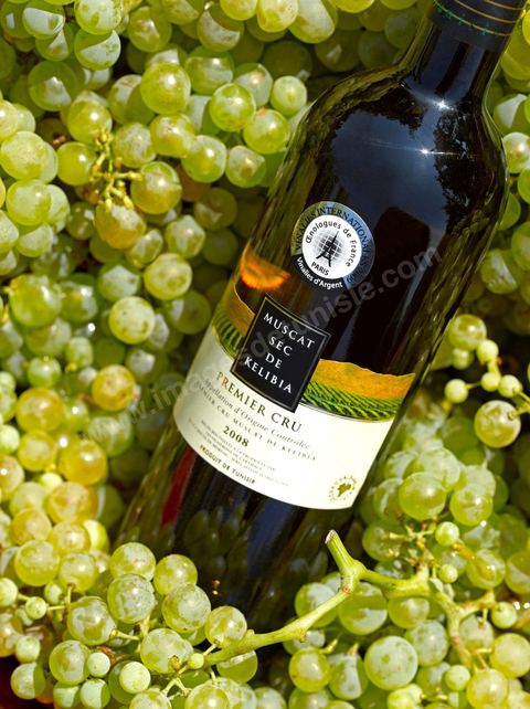 A bottle of dry Muscat white wine from Kelibia sat among clusters of white grapes in the heart of the Kelibia vineyard
