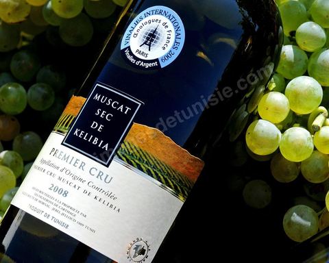 A bottle of dry Muscat white wine from Kelibia sat among clusters of white grapes in the heart of the Kelibia vineyard