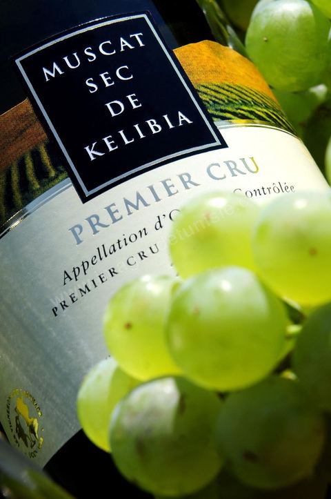 A bottle of dry Muscat white wine from Kelibia sat among clusters of white grapes in the heart of the Kelibia vineyard