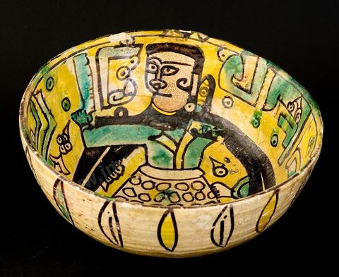 COUPE DE LA DAME EN CAPE NOIREKhorassan, Nichapour, 10 - 11  siècleUn personnage féminin en vêtement ocellé et cape noire à fausses manches pointues, tient à  la main un objet difficile à identifier (hache, miroir ou parchemin).Le thème de la dame debout, à l'oeil étiré (mais vu de profil), tenant un objet, se rencontre dans la céramique 'tunisienne' du 10 siècle. C'est le décor central ornant deux plats dits Dame de Sabra, découverts sur le site fatimide de Sabra Mansouriya et conservés au Musée des Arts Islamiques à Raqqada (Kairouan).