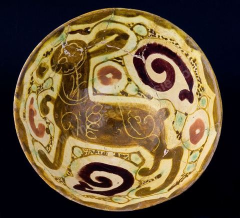 COUPE AU LIÈVRE.Khorassan, attribuée à Nichapour, 10  -11  siècle.Motifs incisés sur le corps du lièvre, entouré de larges volutes, de motifs concentriques et de ponctuations en semis. Le lièvre est un peu l'animal fétiche des arts arabes et musulmans. Il est généralement associé aux thèmes de bon augure, de perspicacité et d'abondance. Il figure en bonne place sur les céramiques fatimides d'Ifrikia (Tunisie) et d'Egypte, (905-1055). Certains chîites s'interdisaient sa consommation en l'associant à la figure de Alî, gendre du prophète Mohammad, et son seul successeur légitime de leur point de vue.