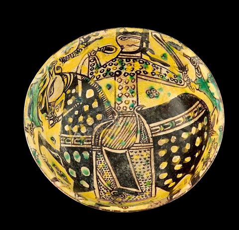 COUPE À DÉCOR DE CAVALIERKhorassan,Nichapour 10 - 11  siècleCoupe creuse caractéristique des céramiques de Nichapourà thème central. Un cavalier tenant une épée sur fond jaune peuplé de quadrupèdes et de volatiles. L'ample harnachement de la monture, traité dans un noir-brun intense et parsemé de points ocellés, suggèreou un thème astral ou l'évocation d'un  personnage de haut rang.