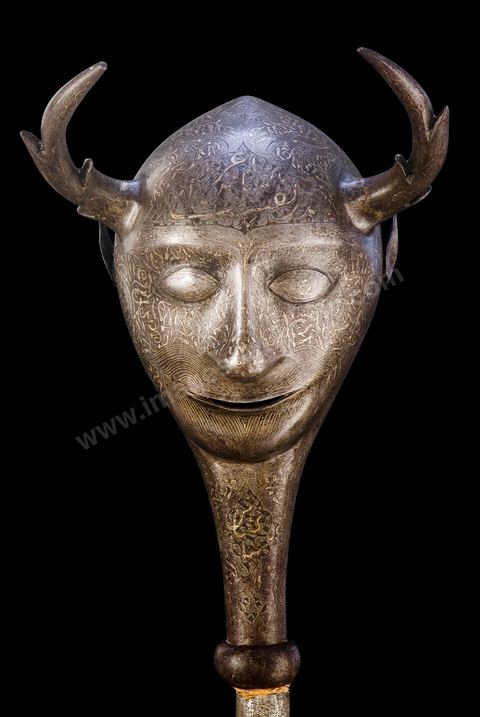 EMBLÈME DE CÉRÉMONIE RELIGIEUSE.Perse, qadjar, 19  siècle. Acier incrusté d'argent.Cette figure représentant un génie malfaisant évoque autant le 'diable' que la part diabolique qui est dans le coeur des hommes. Par extrême piété, certains religieux n'hésitaient pas à l'utiliser comme attribut, rappellant à eux-mêmes et à leurs disciples la fragilité de la condition humaine. Le combat contre le mal est un thème caractéristique du théâtre religieux chîite, le 'tazié '.En Tunisie où règna pourtant une dynastie chîite, les Fatimides, le chîisme ne résista pas face à l'enracinement populaire de l'Islam sunnîte, dit orthodoxe. De ce passé des traces ont néanmoins  subsisté auxquelles il faut additionner une vénération due à la famille du prophète.La figure de 'Alî', gendre du Prophète, ornait jusqu'au milieu du 20  siècle, ex-voto et images populaires. On voyait Alî, muni de son sabre légendaire, livrant bataille à un être hybride, tête à deux cornes, dit 'ras el-ghoul ', 'tête d'ogre'