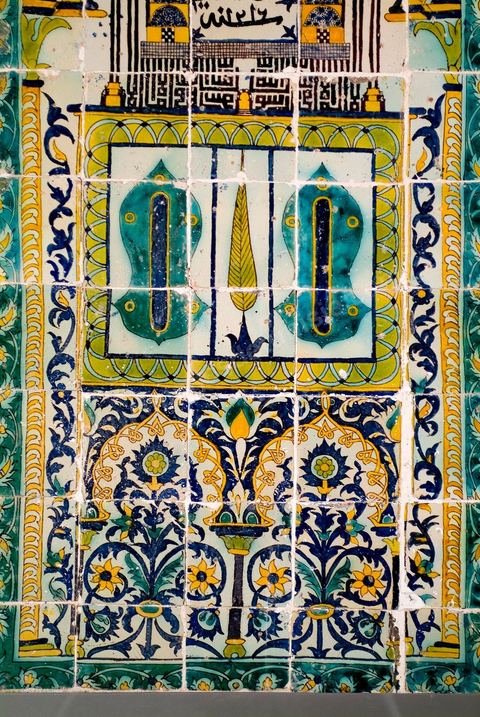 PANNEAU DE CÉRAMIQUE AUX SANDALES DU PROPHÈTE.Tunisie, husseïnide, signé et daté, Khémiri 1216 H./1801Panneau à thème de 'mihrâb', la niche de prière en Islam. Le cadre est orné de rinceaux fleuris de 'lotus' et de feuilles de 'SAZ' ottomanes. Au centre de l'arc, on reconnaît une mosquée à coupole centrale de style ottoman. Six minarets s'élancent, traçant, en graphie coufique à haute hampe, et en miroir, la profession de foi musulmane: Il n'y a de Dieu qu'Allah et Mohammad est son prophète". À leur base se dessine une minuscule porte jaune à claveaux bruns et blancs, donnant une idée de la proportion suggérée. Au centre du mihrâb, de part et d'autre d'une palme, un panneau figurant les sandales du prophète. Au dessous, deux arcs polylobés renfermant une composition florale. La croyance dans les vertus bénéfiques, la baraka, des attributs corporels et vestimentaires du prophète, est encore de nos jours, vivante en Islam. Une sorte de culte est voué à l'empreinte de son pied conservée à Istanbul, et à trois de ses cheveux, enterrés au mausolée de son compagnon, Abou Zamaâ Al Balaoui, à Kairouan, quatrième ville sainte de l'Islam. Du Maroc jusqu'en Inde, les Sandales du prophète ont une place particulièrement éminente, ornant ici les enluminures, là, donnant leur nom à une mosquée. Dans les lieux où elles figurent, elles évoquent la 'visite' ou la 'présence' du prophète. Leur aura assure au lieu protection et patronage. Les cinq motifs en oeilletons, au nombre des doigts de la main, qui ponctuent les sandales, contribuent à la protection et à l'éloignement du mauvais oeil.  La signature de l'artiste, peu courante dans ce genre d'ouvrage et dans l'art  arabe en général, prend, au dessous de la grande coupole, une position centrale, immodeste. Un voeu de piété, le désir d'être enterré auprès du prophète - la mosquée serait celle de son mausolée à Médine -, pourrait la justifier. Protecteur de la demeure 