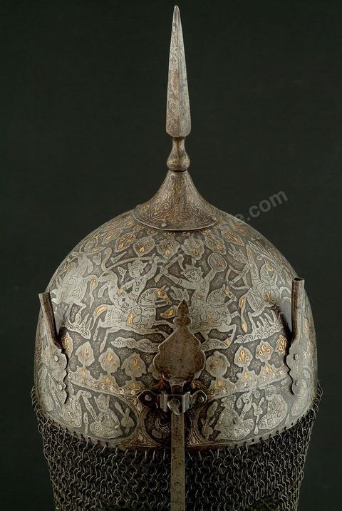 CASQUE DE CÉRÉMONIE.Perse qâdjâre,19  siècle.Acier, Or et Argent.Cette forme, en pointe, est archaïsante et se retrouve dans de nombreuses miniatures à thème guerrier. Le repertoire iconographique, scène de chasse à courre, où abondent les figures humaines et animalières, permet de situer le casque dans la série des armures à usage cérémonial, caractéristique des rites chîîtes. Apporté, vraisemblablement, par les turcs, ce genre de casque se retrouvait en Tunisie. Un casque dit, 'de Rostam' est conservé au Musée Militaire du Palais de la Rose, dans la banlieue de Tunis.	 - Musée Lella Hadria à Djerba Explore