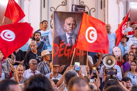 Tunis, Tunisie – 20 août 2026. Des manifestants défilent dans le centre de Tunis contre le président Kaïs Saïed, appelant à son départ et réclamant davantage de libertés politiques et la libération de détenus et opposants. Portraits du président barrés du slogan « DÉGAGE », drapeaux tunisiens et pancartes accompagnent la manifestation. La mobilisation intervient dans un contexte de mécontentement social croissant après plusieurs semaines de fortes chaleurs, de coupures d’eau et d’électricité et de difficultés d’accès à certains médicaments et produits essentiels.