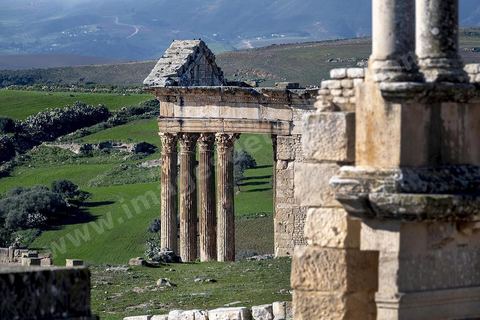 Capitole de Dougga et son majestueux temple. Le site de Dougga, classé au patrimoine mondial de l'UNESCO, Situé sur un éperon dominant la riche vallée de la Mejerdah, le site s'étend sur plusieurs dizaines d'hectares et couvre plusieurs ères historiques. L’excellent état de conservation de la plupart des monuments qui le composent dont certains, tels le capitole ou le théâtre, ont été « remis sur pied » au cours d’une campagne menée au lendemain de la première guerre mondiale par des prisonniers de guerre.