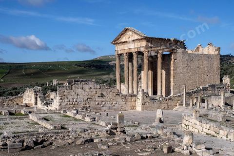 Capitole de Dougga et son majestueux temple. Le site de Dougga, classé au patrimoine mondial de l'UNESCO, Situé sur un éperon dominant la riche vallée de la Mejerdah, le site s'étend sur plusieurs dizaines d'hectares et couvre plusieurs ères historiques. L’excellent état de conservation de la plupart des monuments qui le composent dont certains, tels le capitole ou le théâtre, ont été « remis sur pied » au cours d’une campagne menée au lendemain de la première guerre mondiale par des prisonniers de guerre.