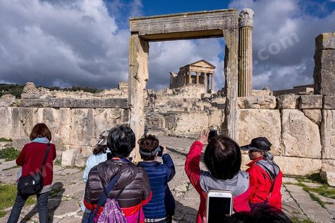 Touristes chinois à dar Lacheb sous fon de temple et capitole. Le site de Dougga, classé au patrimoine mondial de l'UNESCO, Situé sur un éperon dominant la riche vallée de la Mejerdah, le site s'étend sur plusieurs dizaines d'hectares et couvre plusieurs ères historiques. L’excellent état de conservation de la plupart des monuments qui le composent dont certains, tels le capitole ou le théâtre, ont été « remis sur pied » au cours d’une campagne menée au lendemain de la première guerre mondiale par des prisonniers de guerre.