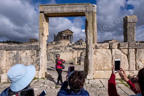 Touristes chinois à dar Lacheb sous fon de temple et capitole. Le site de Dougga, classé au patrimoine mondial de l'UNESCO, Situé sur un éperon dominant la riche vallée de la Mejerdah, le site s'étend sur plusieurs dizaines d'hectares et couvre plusieurs ères historiques. L’excellent état de conservation de la plupart des monuments qui le composent dont certains, tels le capitole ou le théâtre, ont été « remis sur pied » au cours d’une campagne menée au lendemain de la première guerre mondiale par des prisonniers de guerre.