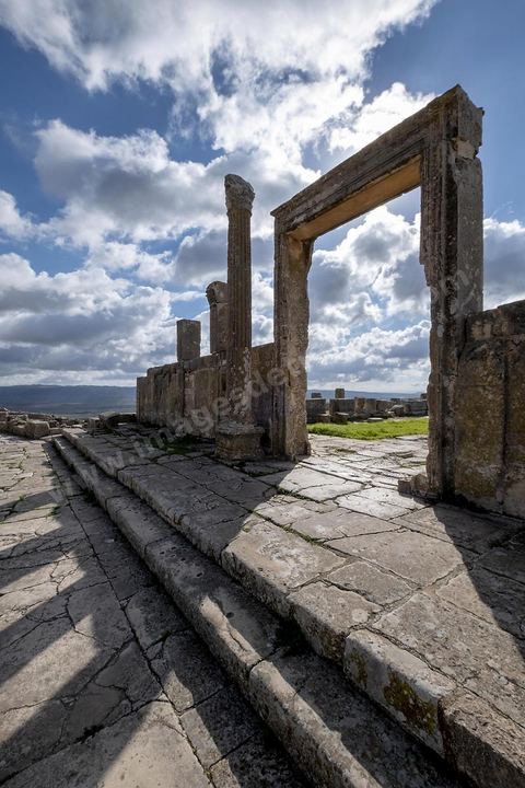 Porte d'entrée de dar Lacheb. Le site de Dougga, classé au patrimoine mondial de l'UNESCO, Situé sur un éperon dominant la riche vallée de la Mejerdah, le site s'étend sur plusieurs dizaines d'hectares et couvre plusieurs ères historiques. L’excellent état de conservation de la plupart des monuments qui le composent dont certains, tels le capitole ou le théâtre, ont été « remis sur pied » au cours d’une campagne menée au lendemain de la première guerre mondiale par des prisonniers de guerre.