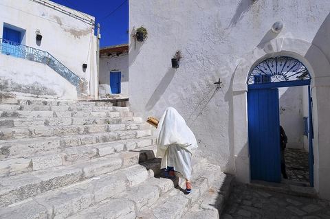 Ruelle de la medina du Kef et porte d'entrée de la synagogue. Femme en safsari revenant de la boulangerie