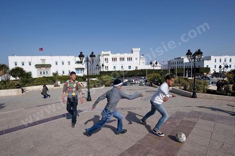 Jeunes lycéens jouant au foot su rla place de la Kasbah avec au fond les Palais du Ministère des Finances et du premier Ministère sur la Place du Gouvernement en haut de la medina de Tunis