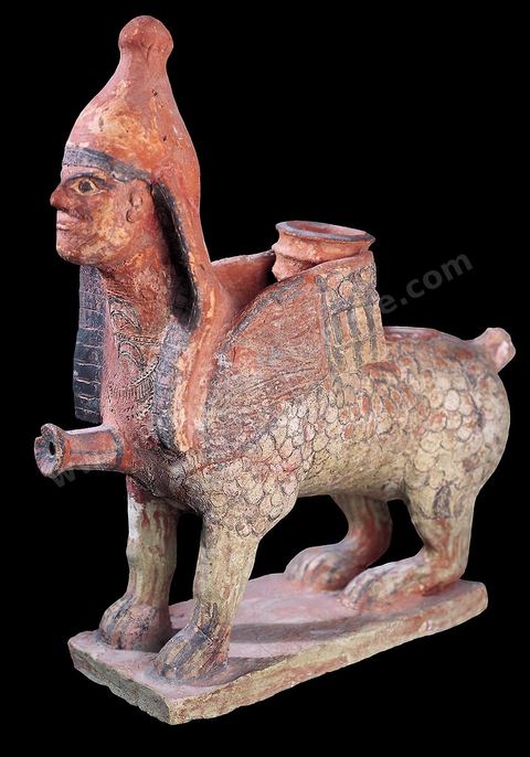 Terracotta vase in the shape of a sphinx. It is topped with a sort of Egyptian pschent in the form of a pointed tiara and has a hole for attaching ornaments. It bears three necklaces around the neck and chest, incised with a drypoint tool before firing (H. 30 cm, W. 32 cm, Archaic Necropolis of Douimès, Carthage, 6th century BCE, Carthage Museum).