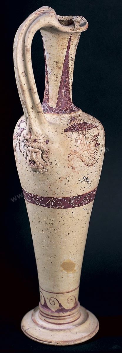 Aiguière en terre cuite ornée d'un décor, dans les tons rouges, varié et d'une grande finesse: en bas de minces filets circulaires et une ligne de flots; au milieu une large bande ornée de rinceaux; autour de la panse, une branchge d'arbuste à feuille s termine par une fleur. Le bas de l'anse repose sur la tête en relief d'un personnage portant une chevelure, une barbe et des moustaches opulentes.  (H. 31 cm, nécropole des rabs, Carthage, IV siècle av. JC, musée de Carthage)