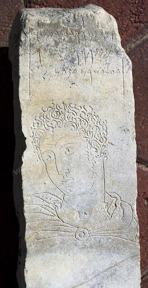 A votive stele made of gray limestone bearing an inscription, beneath which is engraved the face of a teenager clad in a chlamys, whose still, distant gaze seems to be questioning the invisible world. The remarkable intensity of the expression can be compared to Greek or Hellenistic art (H. 75 cm, W. 16 cm, 3rd century BCE, Tophet, Carthage, Carthage Museum)
