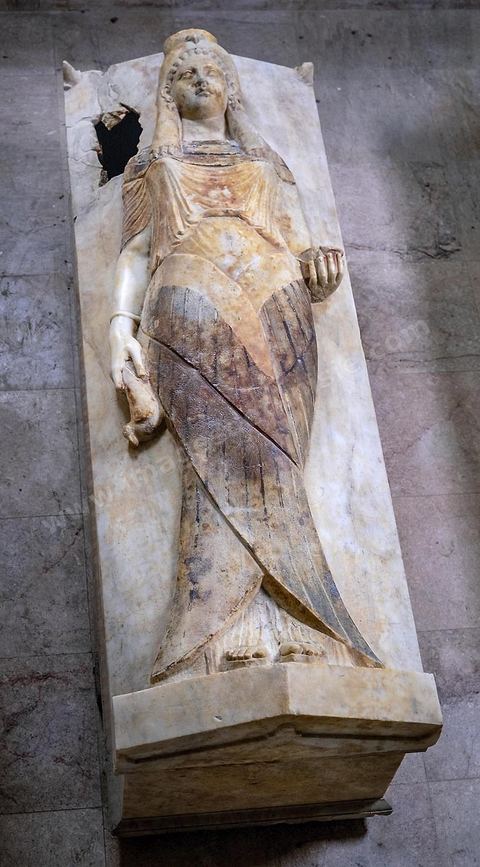 A sarcophagus known as the “Priestess’s Sarcophagus,” made of white marble and decorated with a female figure in high relief. She wears a long pleated robe cinched at the bottom by two large crossed wings. A veil topped with a falcon’s head covers her head in the style of the Klaft. In her right hand she holds a dove, and in her left, an incense burner (H. 93 cm, L. 193 cm, W. 67 cm; Necropolis of Saint Monica, Carthage; 3rd century BCE; Carthage Museum).