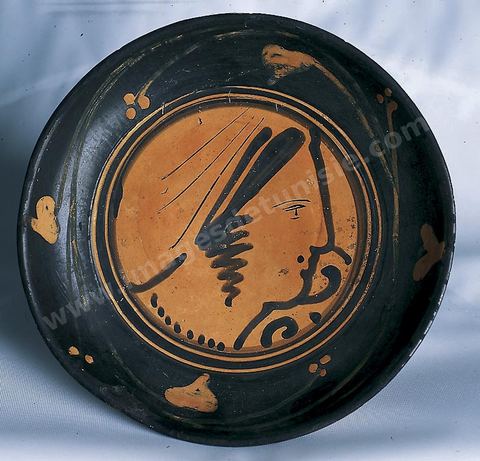 A red-figure plate known as the "Genucilia" plate, believed to originate from Caere (a major Etruscan city), decorated with a female head seen in profile (late Etruscan, 4th century B.C., Carthage Museum).
