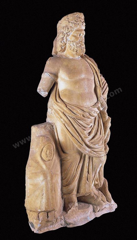 Marble sculpture depicting Aesculapius and Telesphorus. Aesculapius, recognizable by the serpent coiled around a staff, is depicted bare-chested and wearing a modius. Telesphorus, a healing god worshiped alongside Aesculapius, wears a garment with a hood covering his head, Carthage Museum