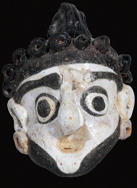 Masques-pendentifs en pâte de verre de différentes couleurs (gris et bleu, blanc et noir, bleu et jaune). Fortement typés, ils ont des yeux exorbités dont l’iris est dilaté et des cheveux et une barbe souvent calamistrés en forme de tortillons. Une bélière permet de les enfiler dans des colliers ou de les porter comme pendentifs. Leur grande vogue se situe aux IVe‑et‑IIIe‑siècles (H.4‑à 6‑cm, nécropoles de‑Carthage, IVe-IIIe siècle av. J.-C., musées du Bardo). Section punique - musée du Bardo