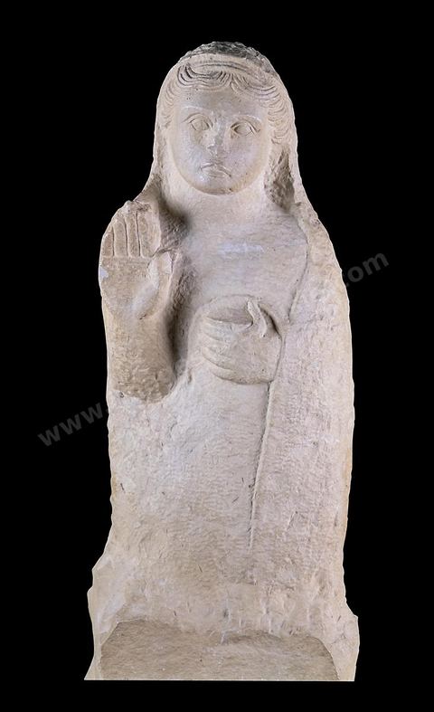 A funerary stele in the form of a statue depicting a female figure standing on a pedestal. A veil draped over the back of her head envelops almost her entire body; the carefully rendered hair suggests an Archaic Greek influence. Her right hand is raised in prayer, while her left holds a pyxis. This stele was erected above the burial shaft of a tomb in Carthage (H. 73.5 cm, Borj Jedid Necropolis, Carthage, 4th–3rd centuries B.C., Bardo Museum). Punic section—Bardo Museum